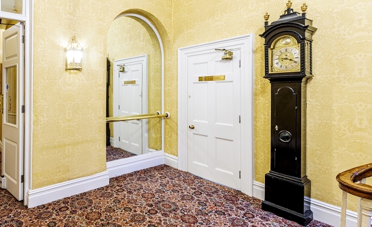 A small room with a wall-length mirror, door and grandfather clock.